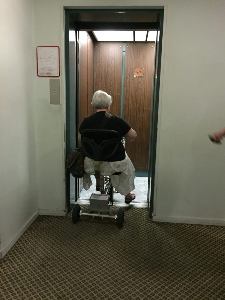 a woman riding a 3 wheel mobility scooter into a small elevator