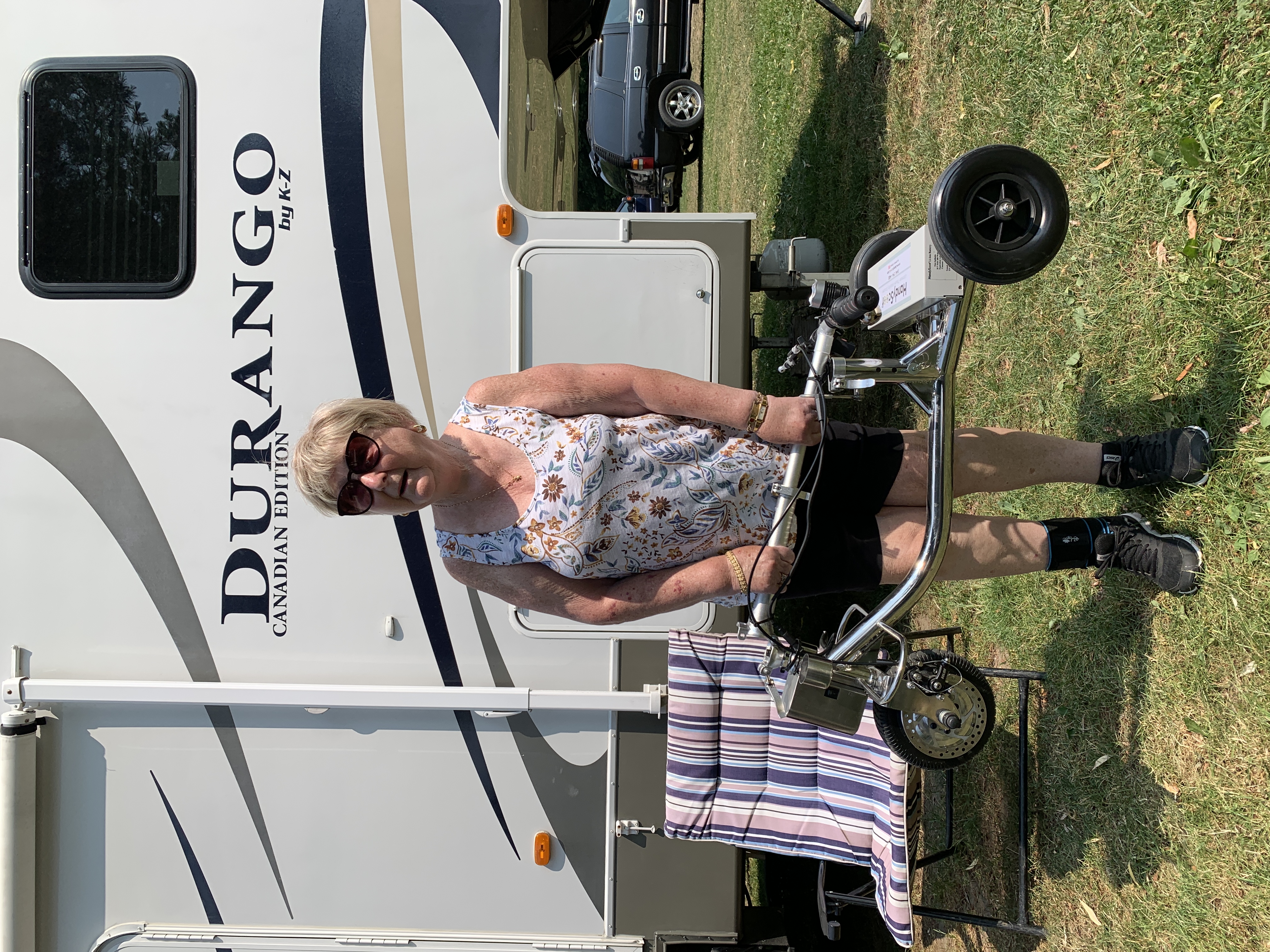A woman lifting a folded mobility scooter near an RV trailer
